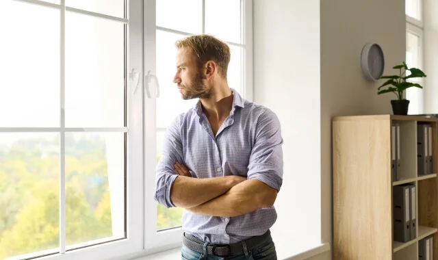 Founder standing in a light-filled room leaning against a window, founder mental health