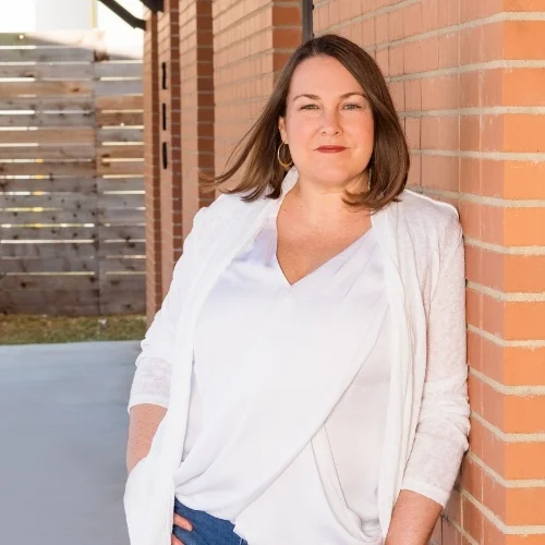 Sonya Stattmann standing against a red brick wall, wearing a white shirt
