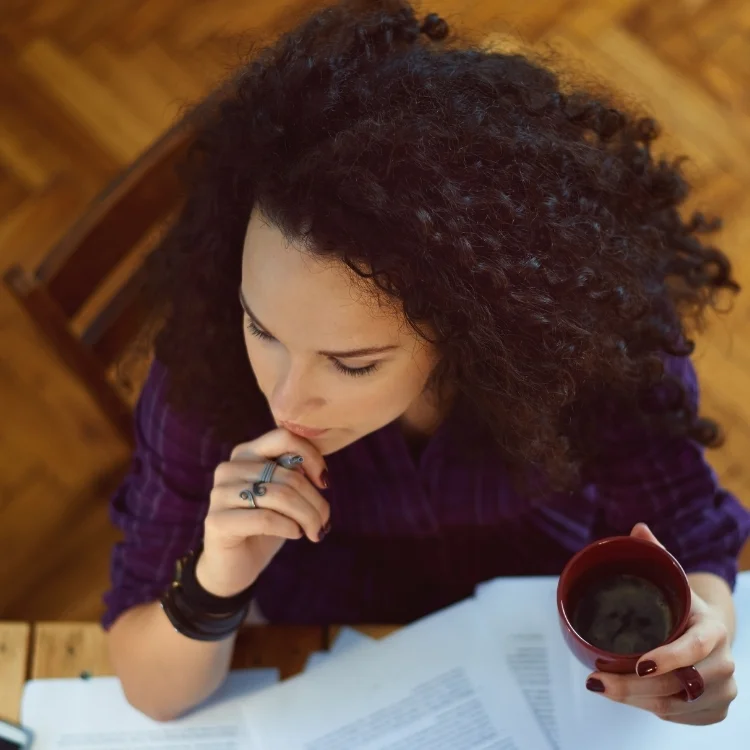 Woman in business at desk with coffee and papers looking contemplative representing the women in business hub