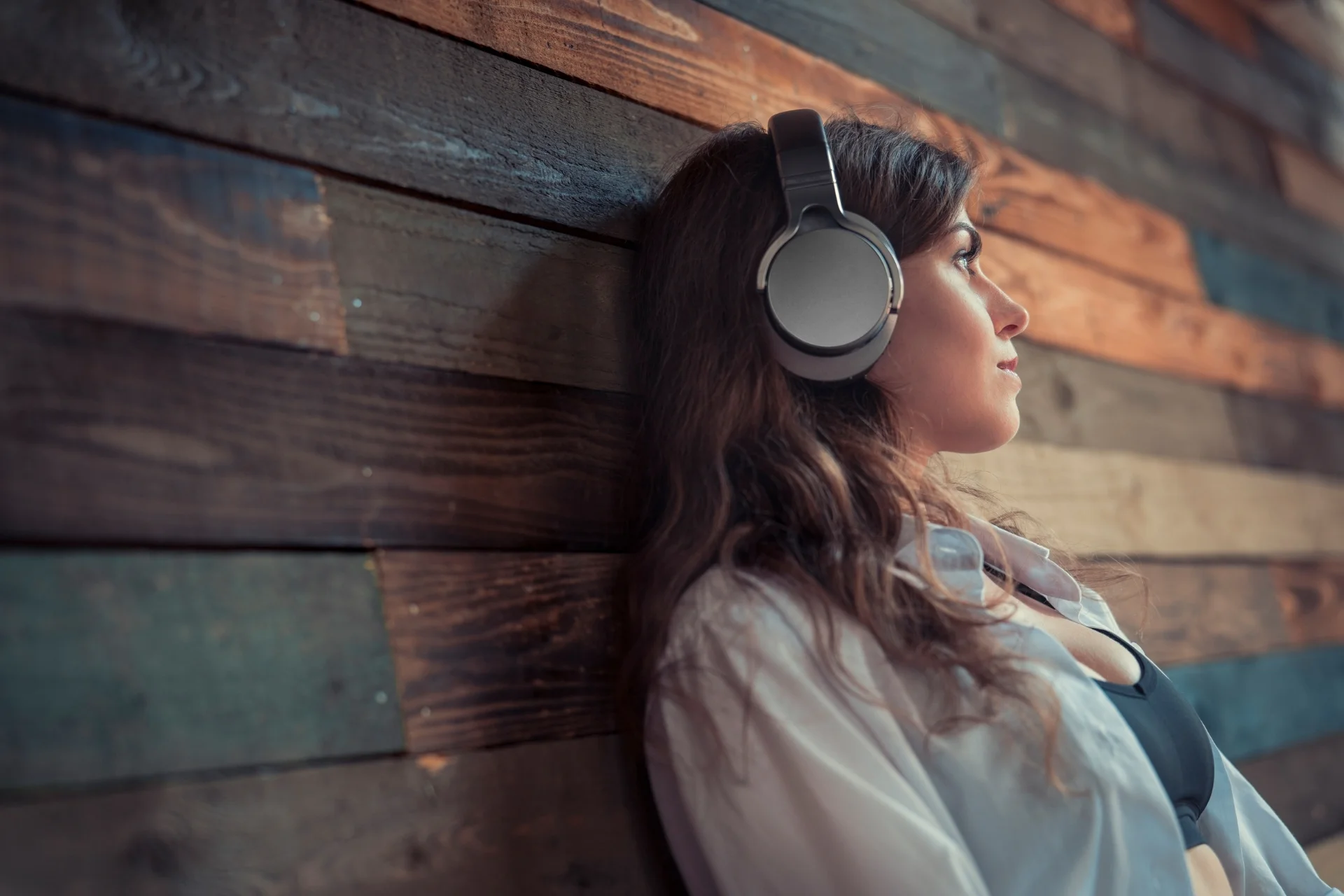 Woman leaning against wood wall listening to nervous system burnout recovery toolkit on headphones mobile version