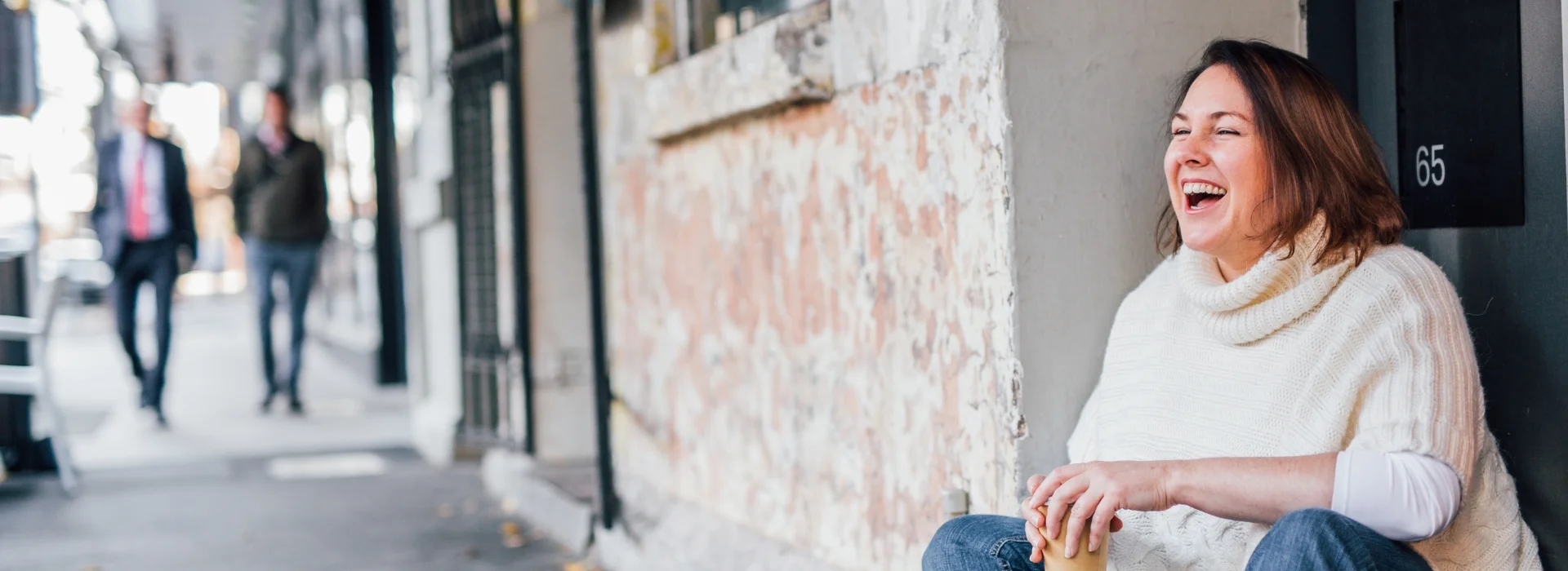 sonya stattmann sitting on kerb with coffee in hand laughing